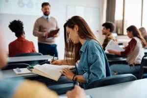 University,Student,Writing,In,Her,Notebook,While,Attending,A,Lecture